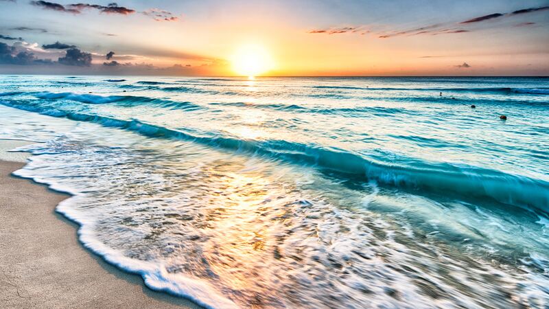 Sunrise over the ocean with waves rolling onto a sandy beach